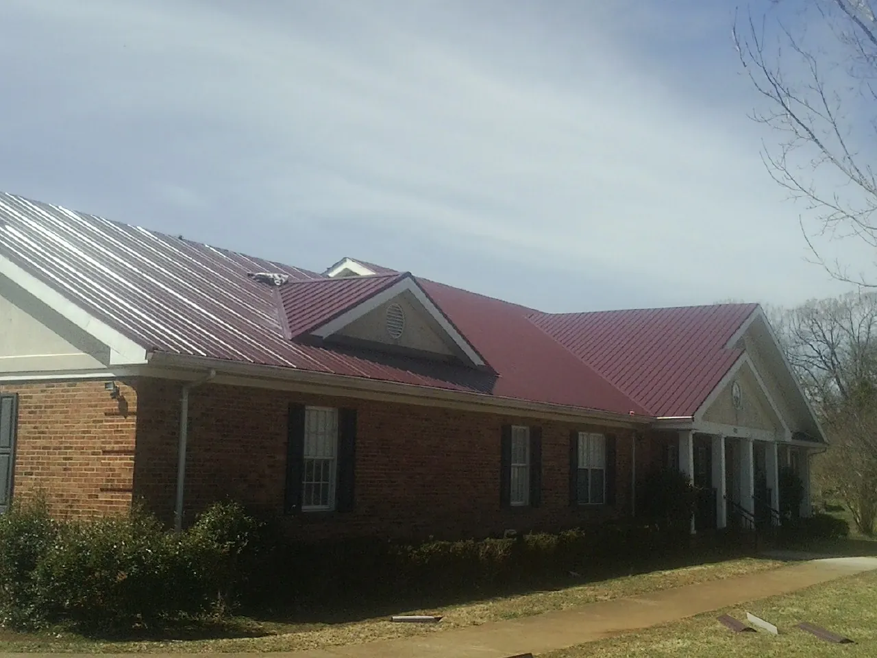 Red metal roof with gabled entries on a long brick building, from a Hail Damage Roof Repair job in Ponsford