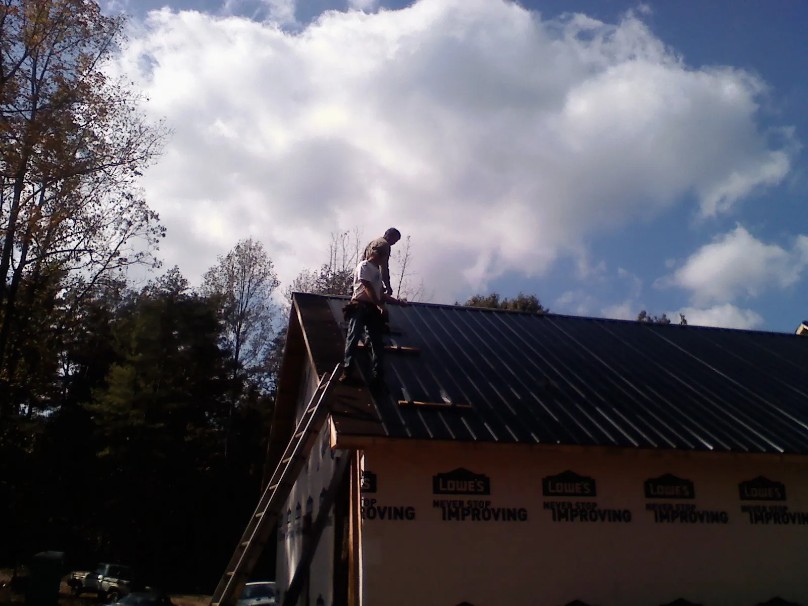 Roofer fastening dark metal panels high against a cloudy sky, from a Roof Inspection job in Ponsford