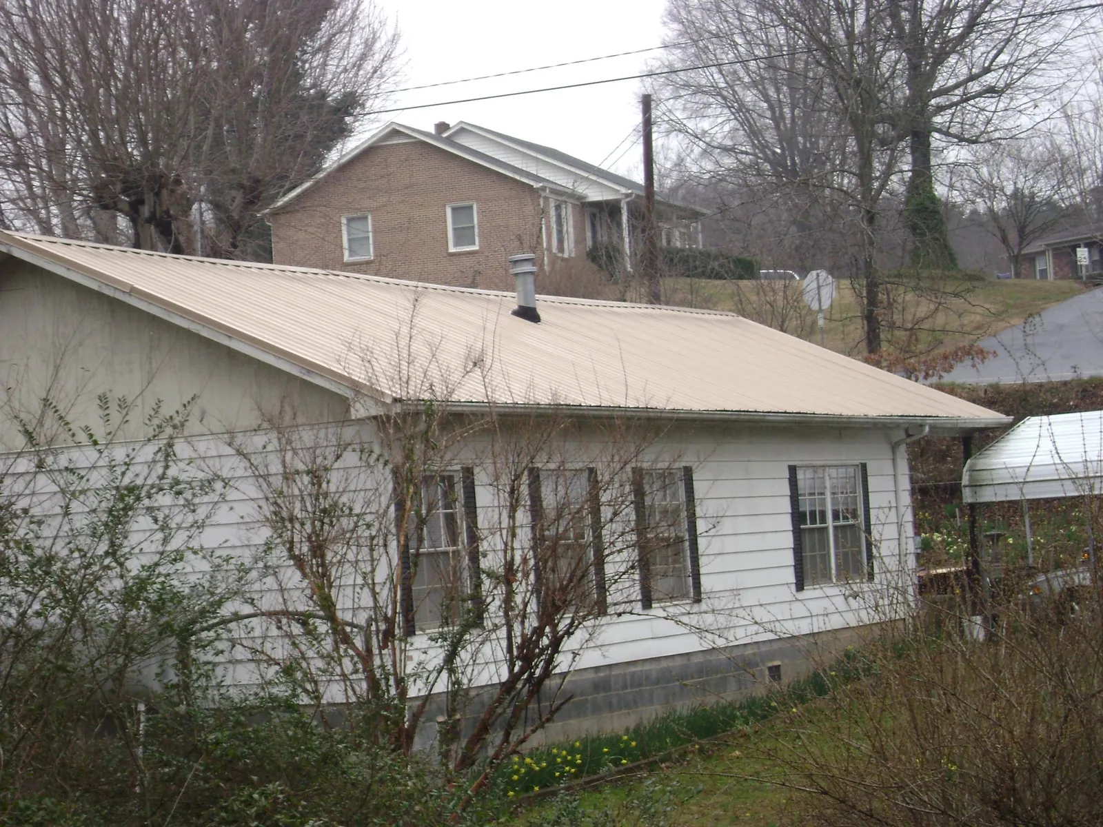 Tan metal roof on a white sided house set into a hillside — Commercial Roofing by Roofing Brothers in Ponsford