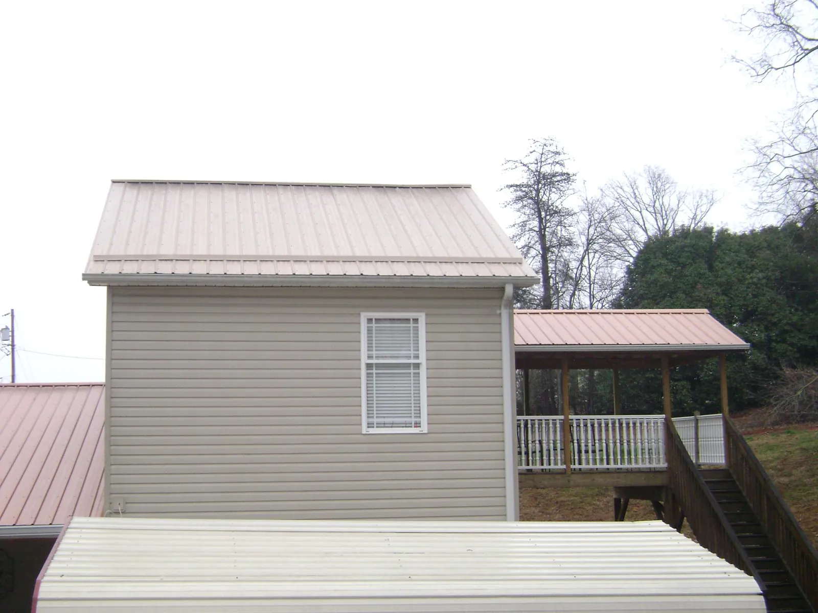 Tan metal roofs on a two story addition and attached porch, from a Roof Replacement job in Ponsford